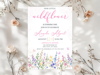 Digital Wildflower 1st Birthday invitation template. Watercolor meadow flowers in purple, pink and blue with butterflies. Text reads "Our Little Wildflower is turning one". Editable Canva template mockup.
