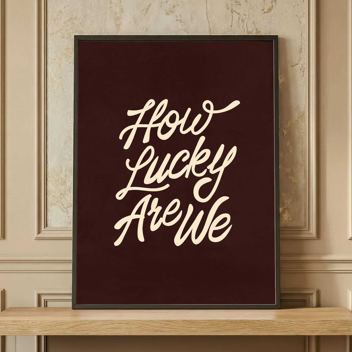 Framed 'How Lucky Are We' typography print in dark brown and cream, retro aesthetic wall art resting on a wooden shelf