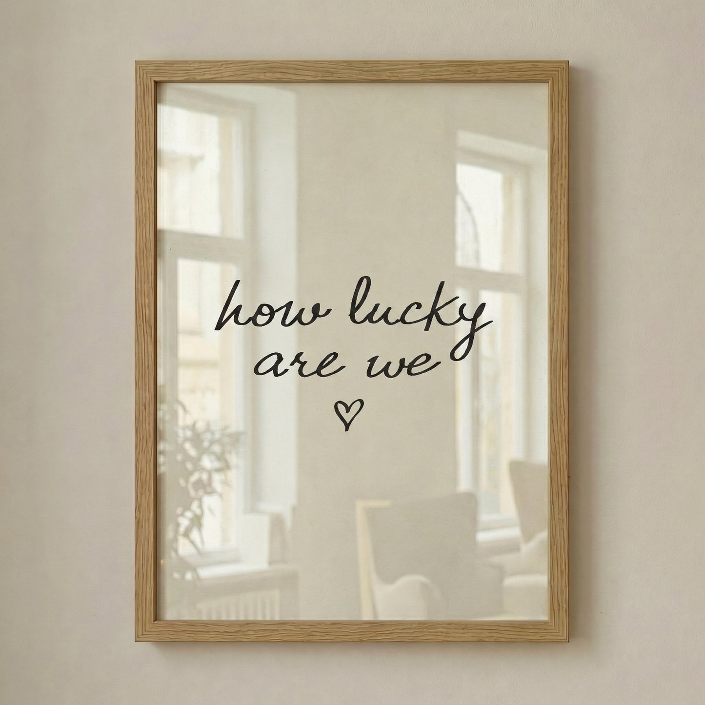 Minimalist typography print saying how lucky are we with a small heart, placed in a light wood frame leaning against a white wall.