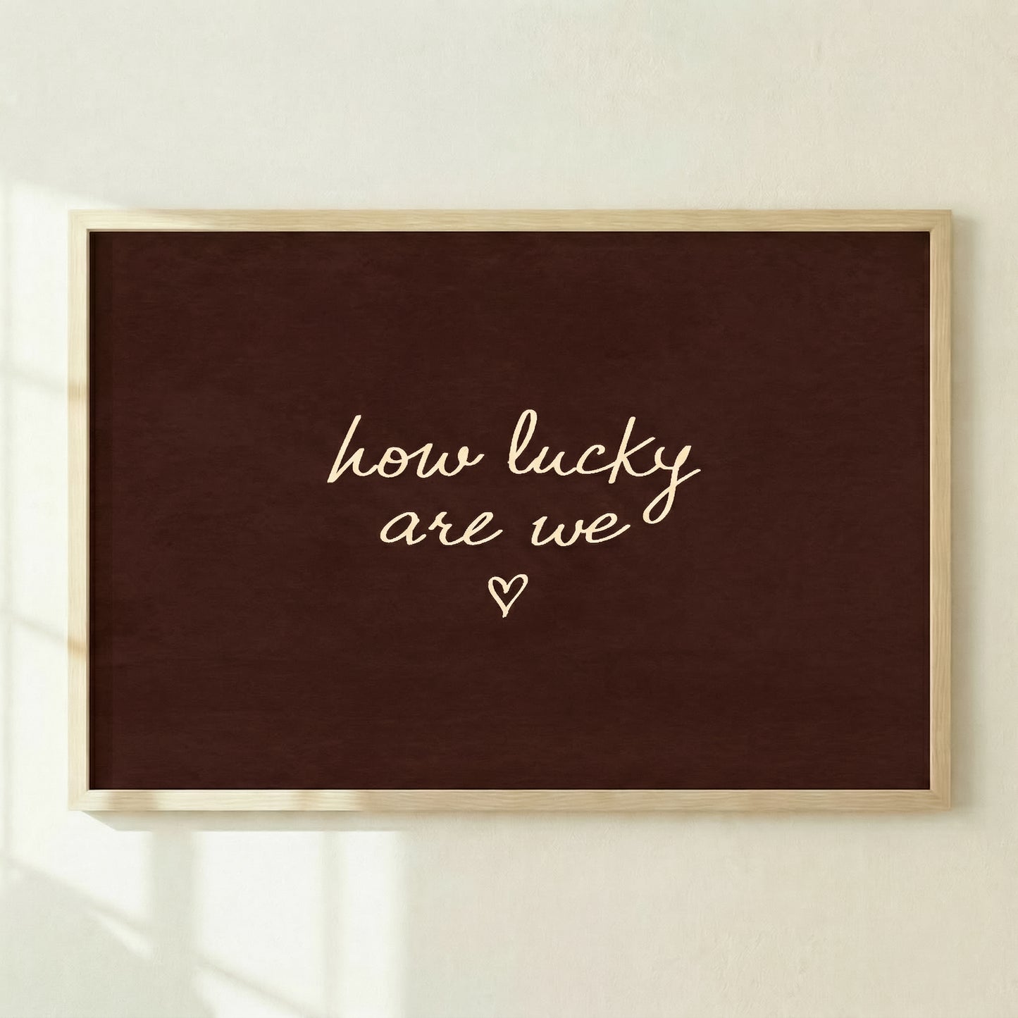 Large dark brown horizontal print reading "how lucky are we" leaning against a concrete wall in a modern living room