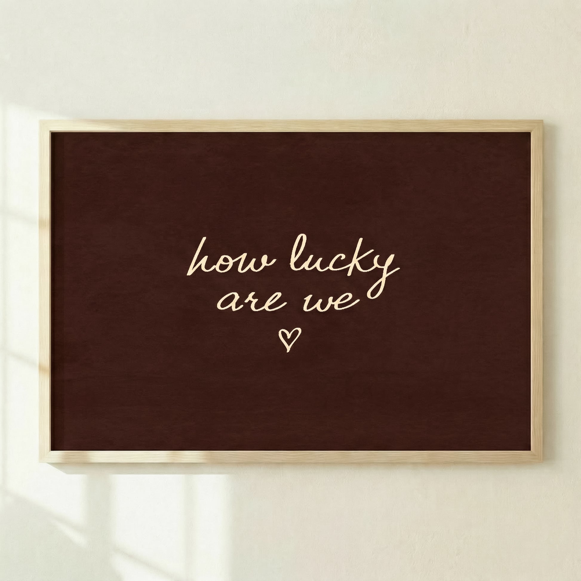 Large dark brown horizontal print reading "how lucky are we" leaning against a concrete wall in a modern living room