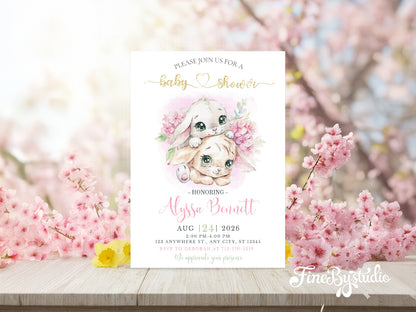 Whimsical baby shower invitation featuring two cute watercolor bunnies surrounded by pink cherry blossoms and gold glitter text.
