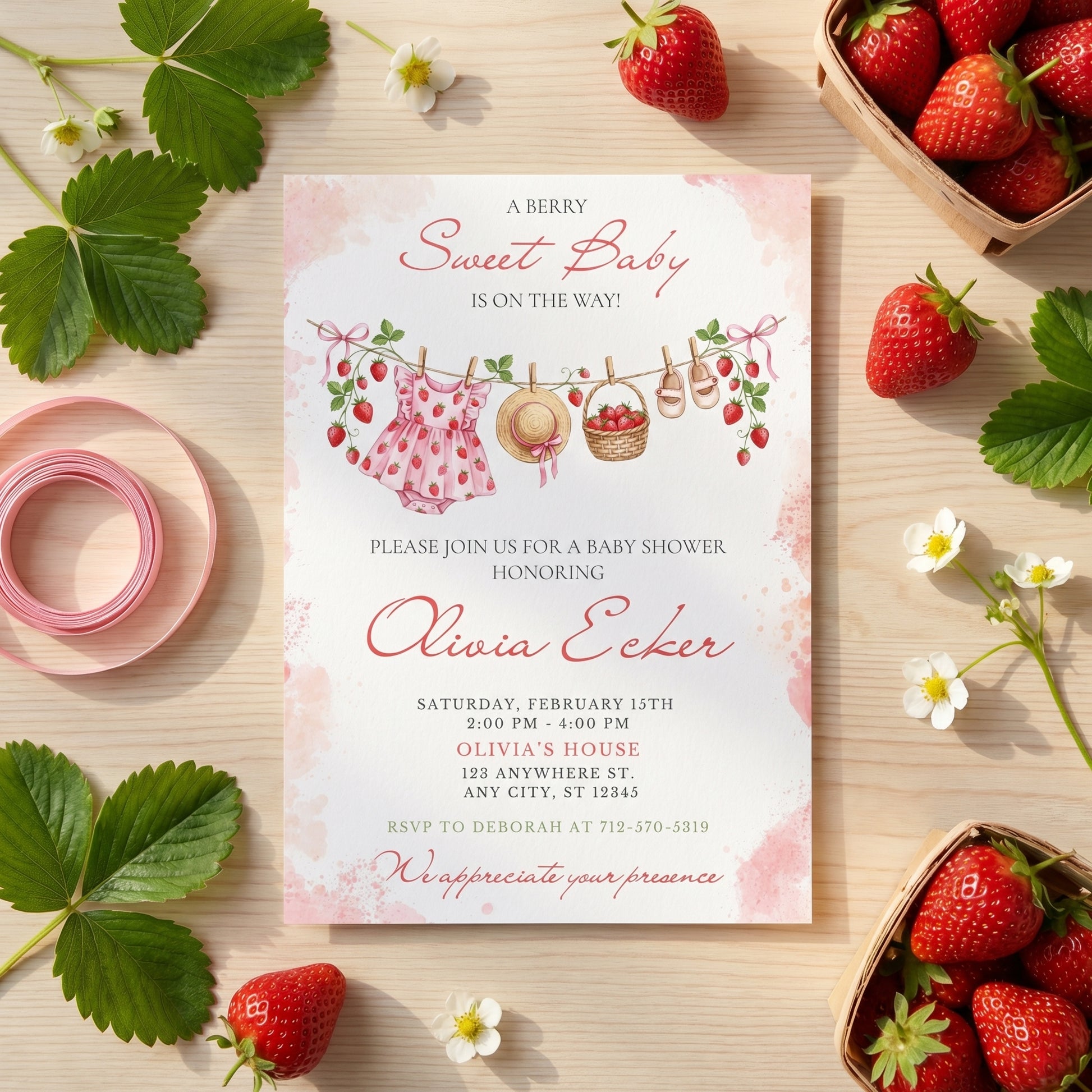 Printed strawberry baby shower invitation displayed on a table next to fresh strawberries, a daisy flower, and pink ribbon.
