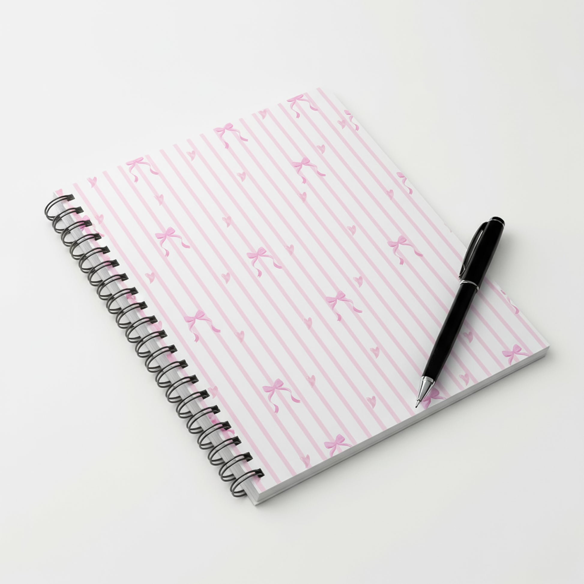 A spiral notebook resting on a table featuring a pink diagonal stripe pattern cover.