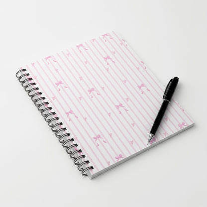 A spiral notebook resting on a table featuring a pink diagonal stripe pattern cover.