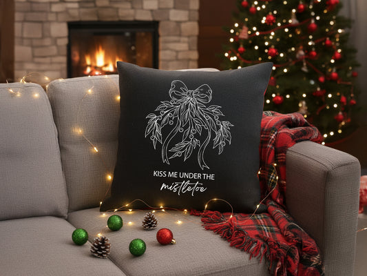 Black holiday throw pillow with white mistletoe vinyl design on a sofa.
