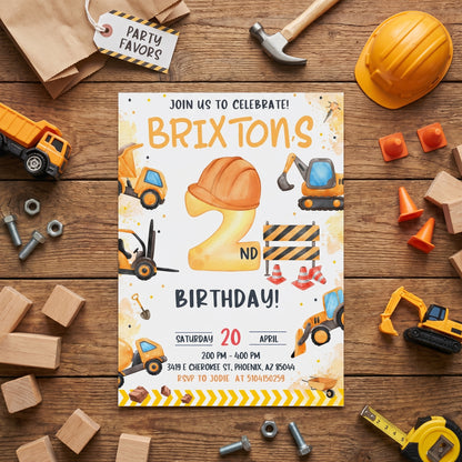 Printed construction birthday invitation displayed on a wooden table with toy dump trucks, hard hat, and caution tape.
